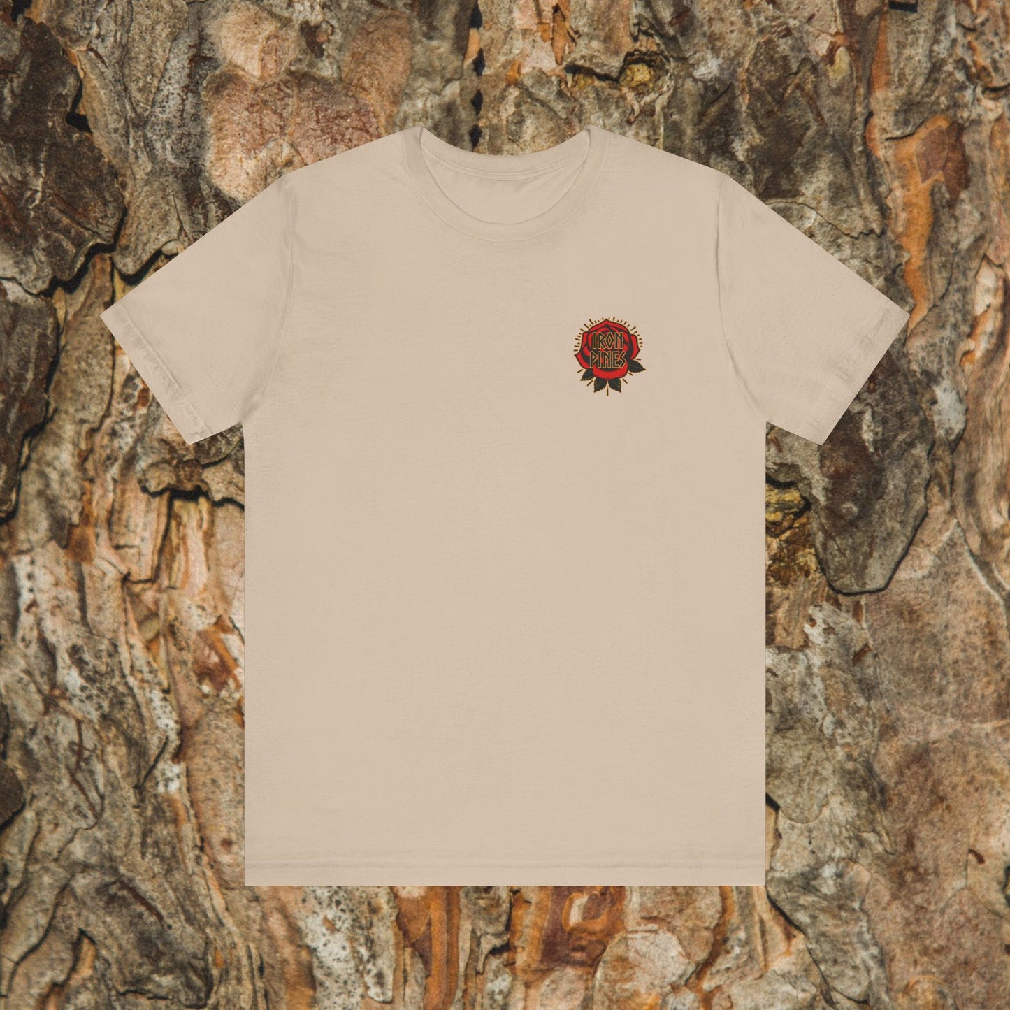 The Never Mistake My Kindness For Weakness unisex beige graphic tee by Printify features a small red and black circular design on the left chest, shown against a textured tree bark background.
