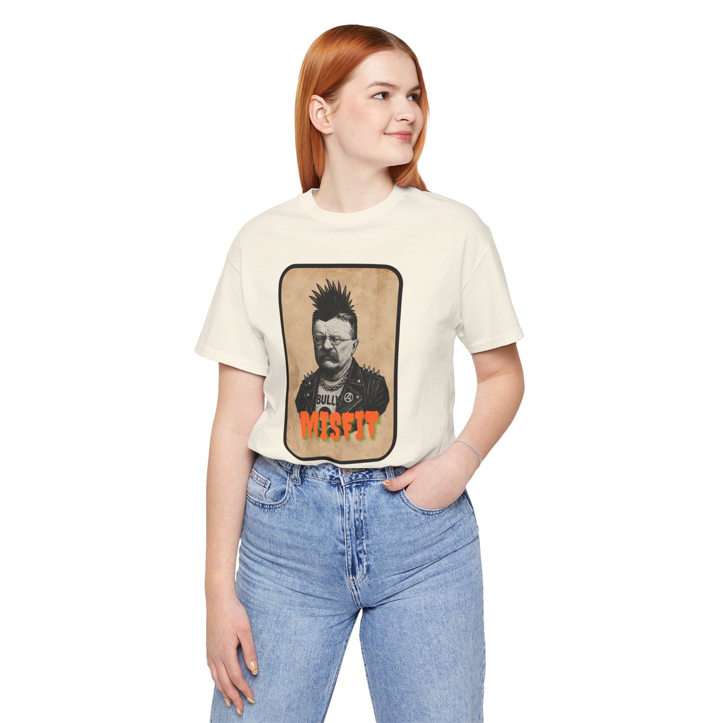 A woman with long red hair, wearing the Iron Pines Teddy Roosevelt Punk T-Shirt from Misfit History, stands smiling with one hand in her pocket. She pairs the white rebel-inspired tee with light blue jeans for a relaxed look.
