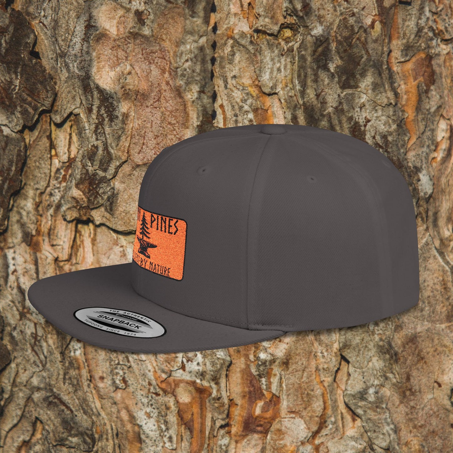 The Iron Pines Logo Hat by Printify features a gray structured snapback with an orange Pines, Happy by Nature patch and tree graphic, shown against a tree bark background—ideal for fans of the Iron Pines collection.