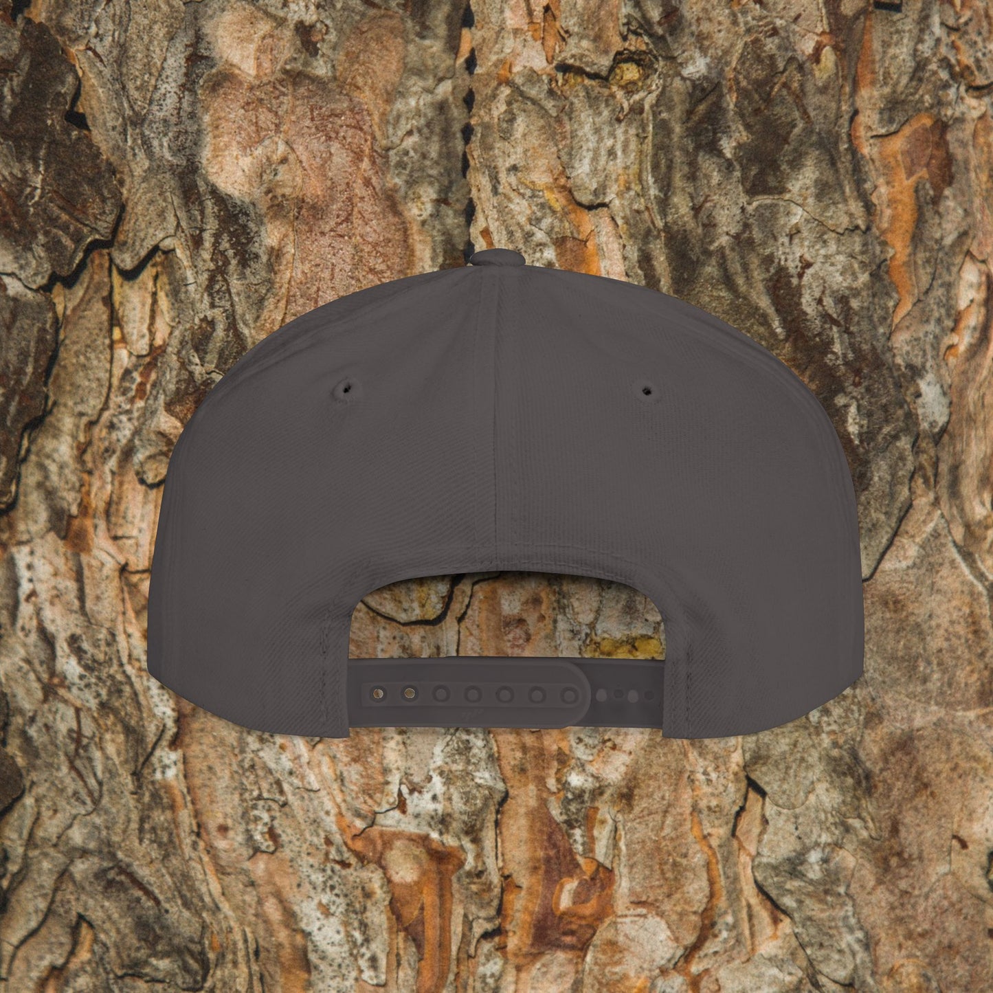 The Iron Pines Logo Hat by Printify is a dark gray structured snapback with an adjustable closure and embroidered logo, shown from the back against textured tree bark.