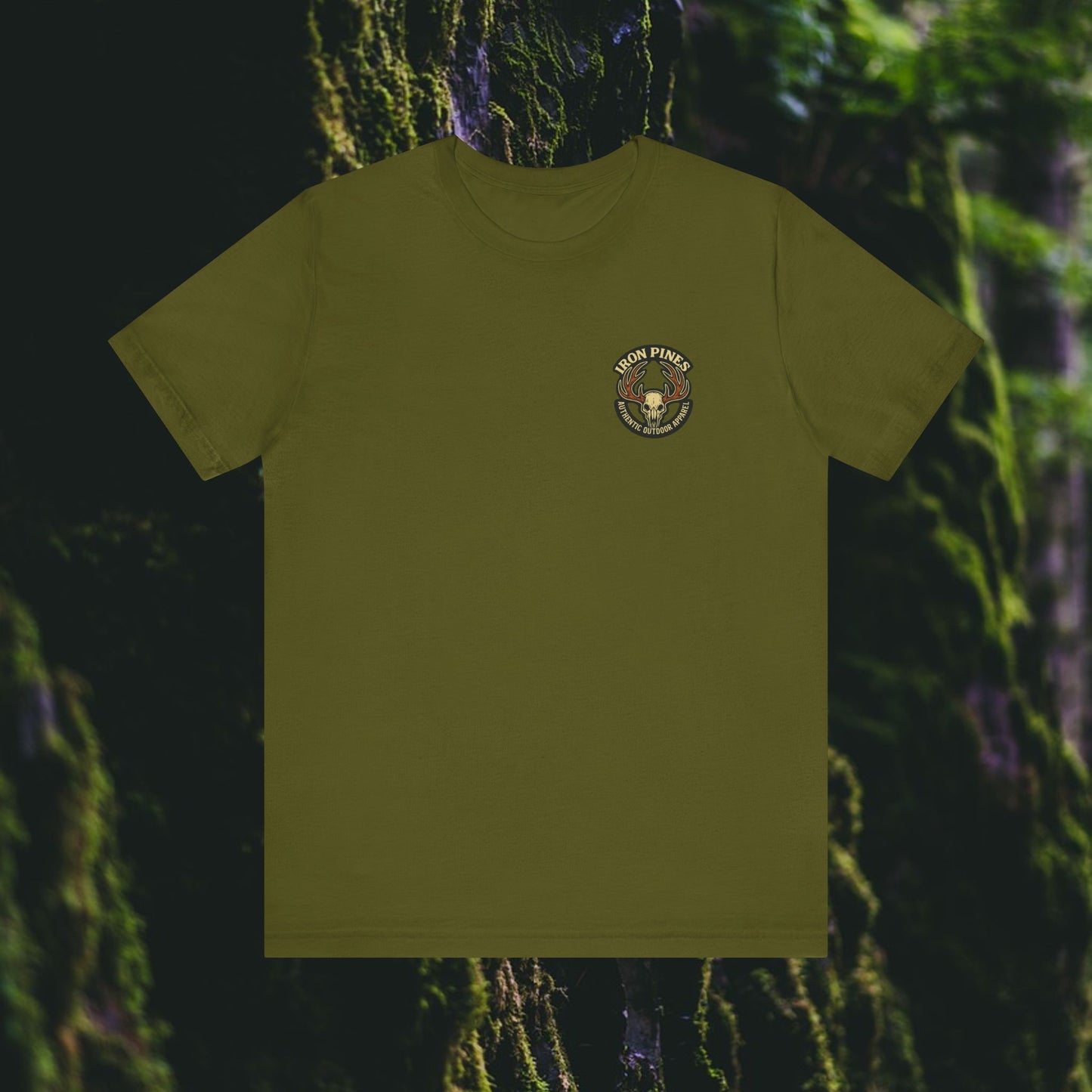 The Printify I Hunt Because Bail’s Expensive Tee – Iron Pines Original is an olive green unisex t-shirt featuring a small, circular Twin Pines Conservation Corps logo on the left chest, displayed against a blurred mossy forest background.