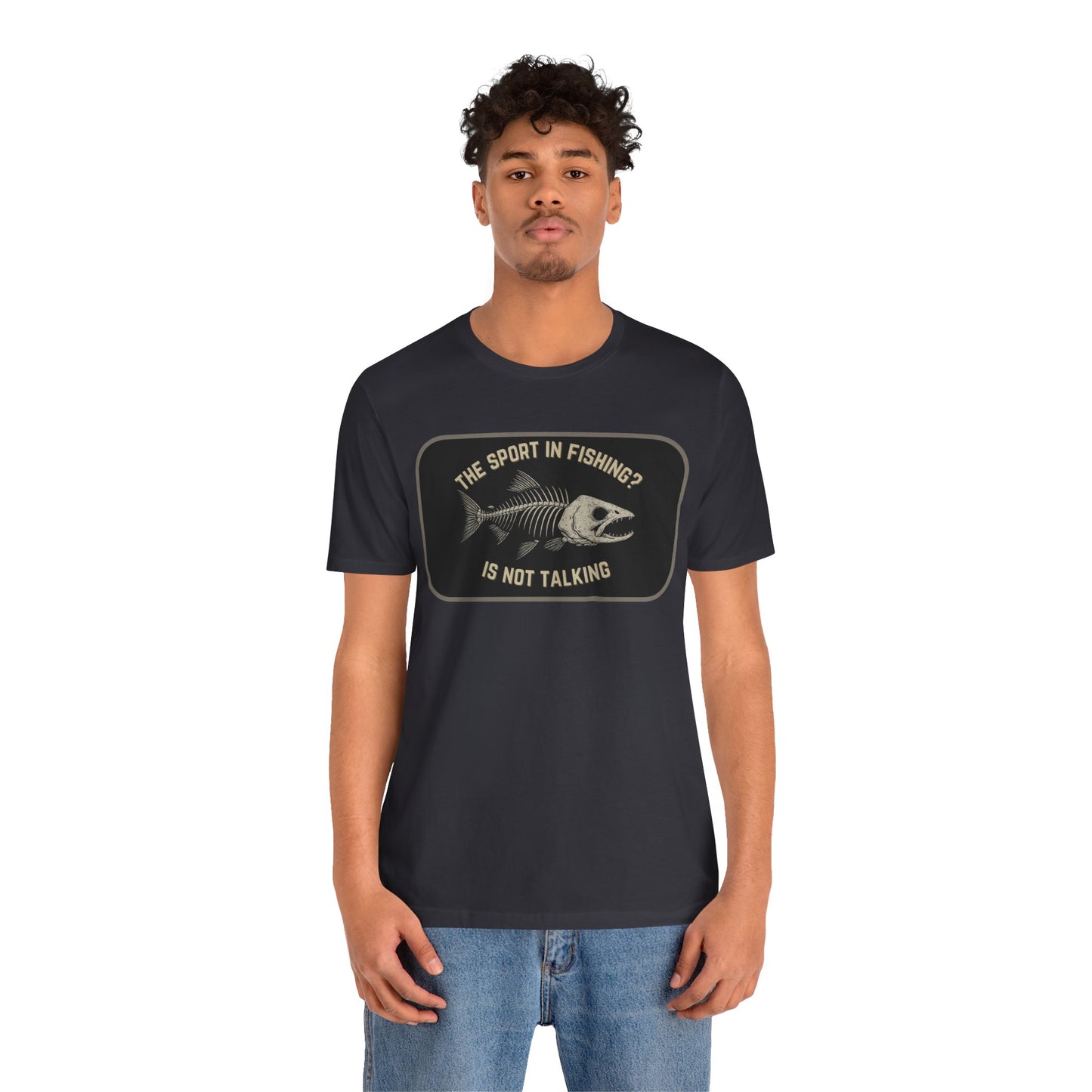 A man with curly hair wears Printify’s “The Sport in Fishing?” Tee, a black unisex shirt featuring a distressed fish skeleton and the phrase “The sport in fishing? Is not talking,” standing against a plain white background.