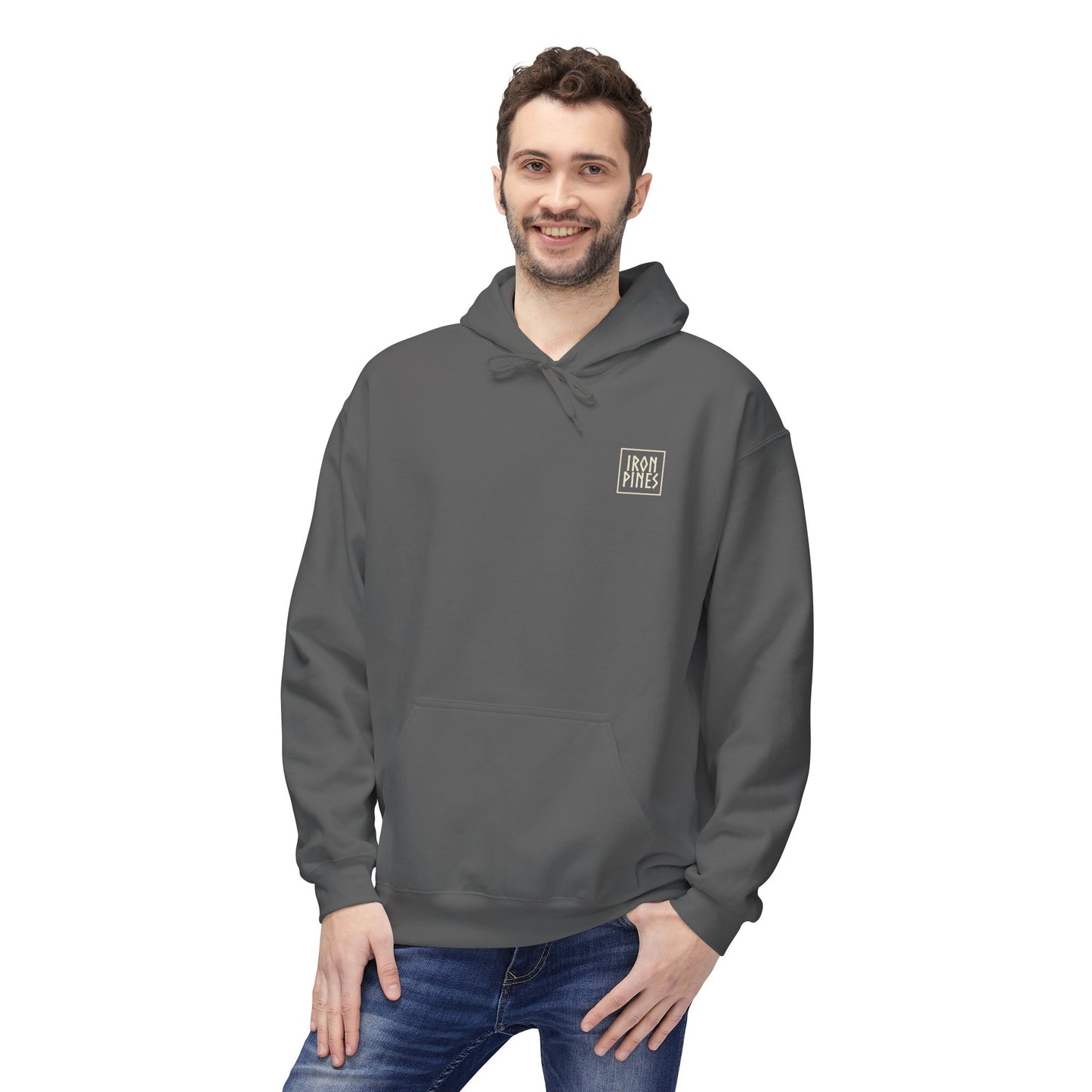 A man with short curly hair and a beard smiles while wearing The Iron Pines Hoodie by Printify, a gray midweight fleece with a small white logo on the chest, showcasing sustainable outdoor apparel against a white background.