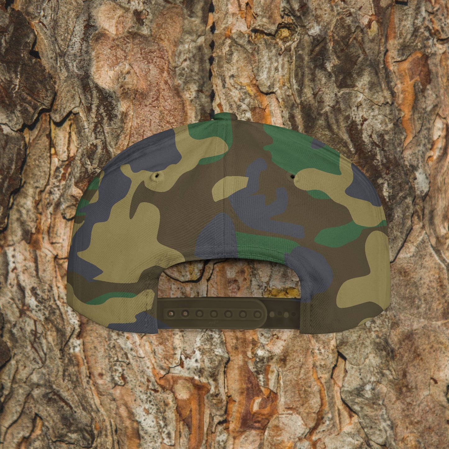 The Iron Pines Logo Hat by Printify, a camouflage structured snapback, is shown from the back against textured tree bark in brown, tan, and green that complements the cap’s pattern and embroidered logo.