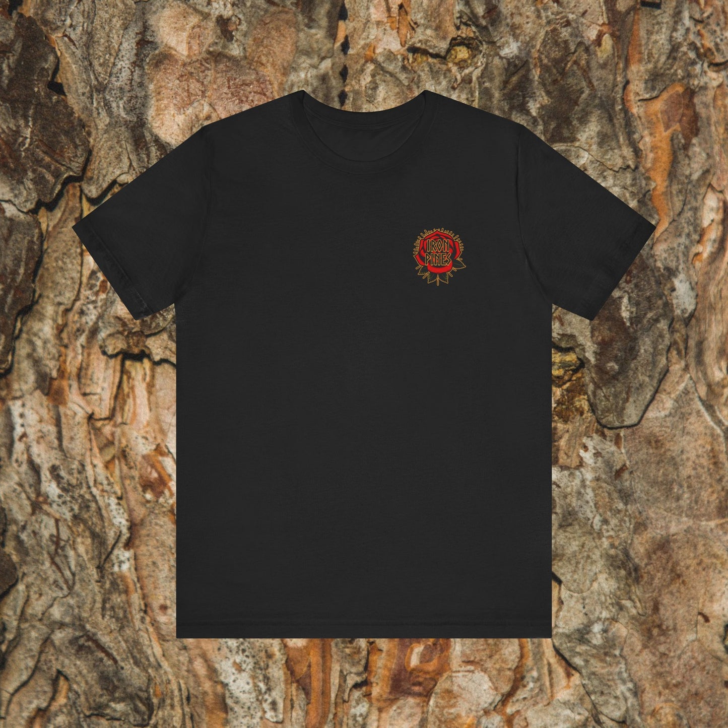 The Never Mistake My Kindness For Weakness Tee by Printify is a black unisex graphic t-shirt with a small circular red and yellow design on the left chest, shown against a textured bark background.