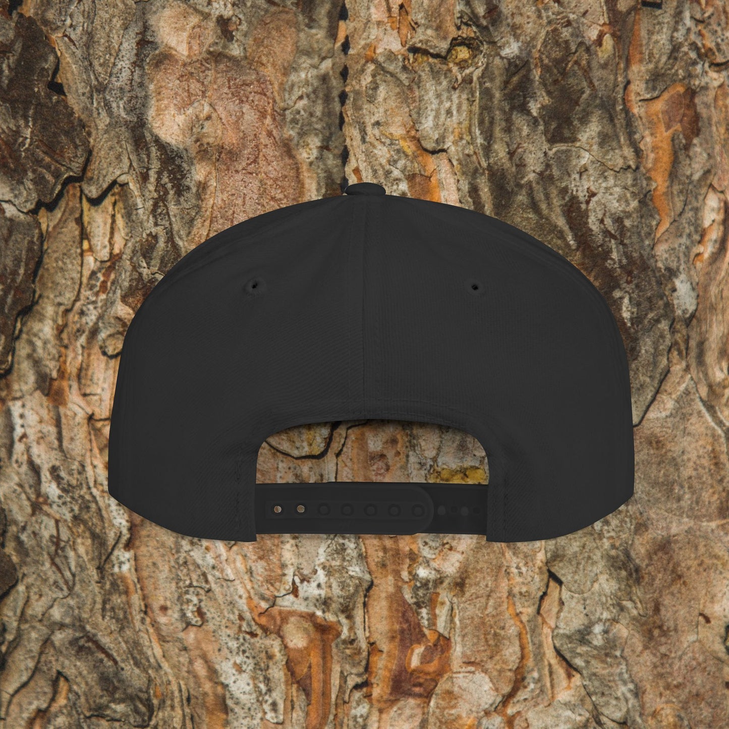 The Iron Pines Logo Hat by Printify is a black structured snapback with an adjustable strap and embroidered logo, shown from the back against textured tree bark.