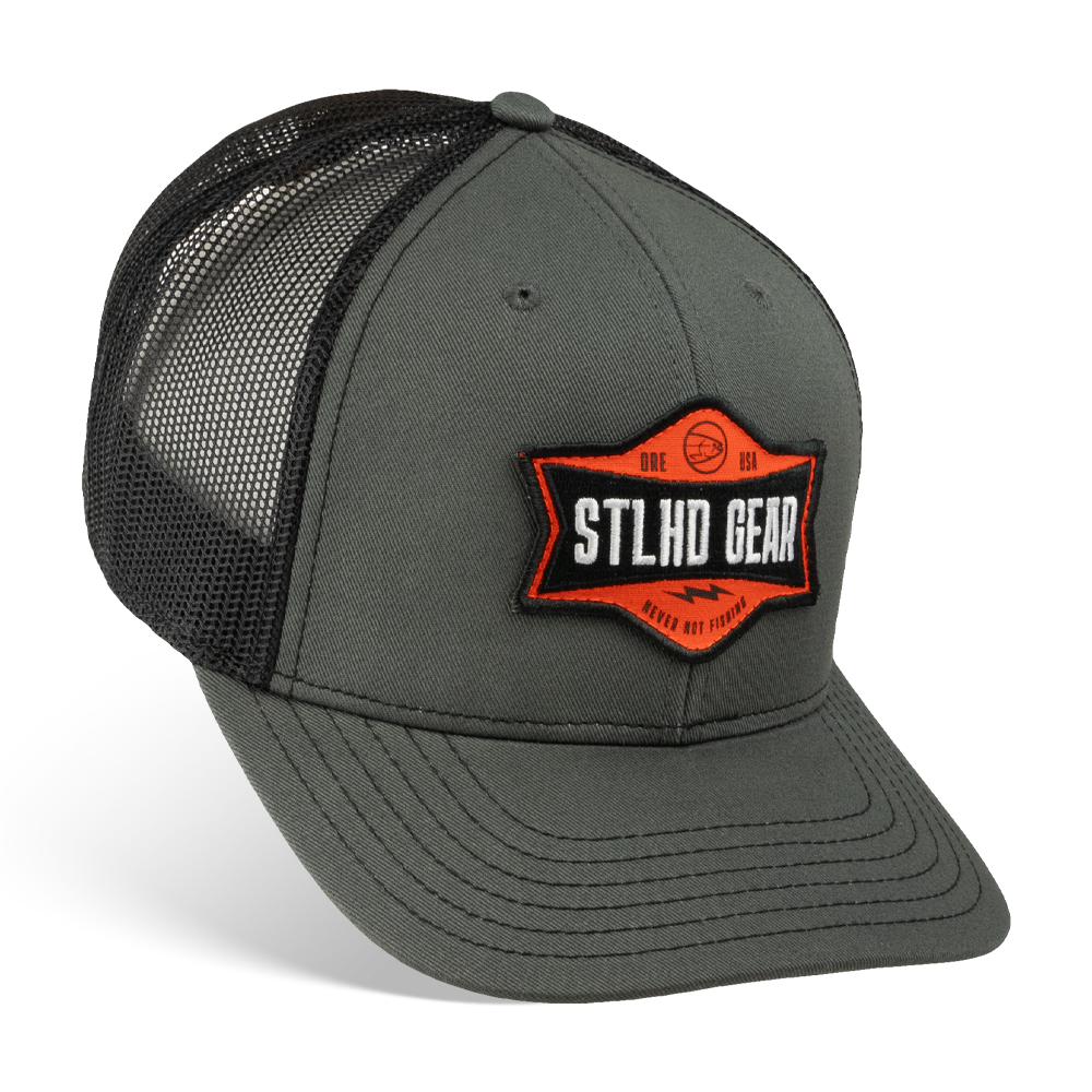 The STLHD GEAR Never Not Fishing Trucker Hat features solid gray front panels, black mesh sides and back, a curved bill, an adjustable snapback closure, and an orange, black, and white STLHD Gear patch on the front.