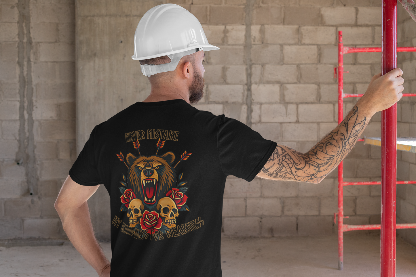 A man in a white hard hat and black Printify Never Mistake My Kindness For Weakness Tee stands at a construction site. The graphic features a roaring bear, roses, skulls, arrows, and the phrase Never mistake my kindness for weakness.