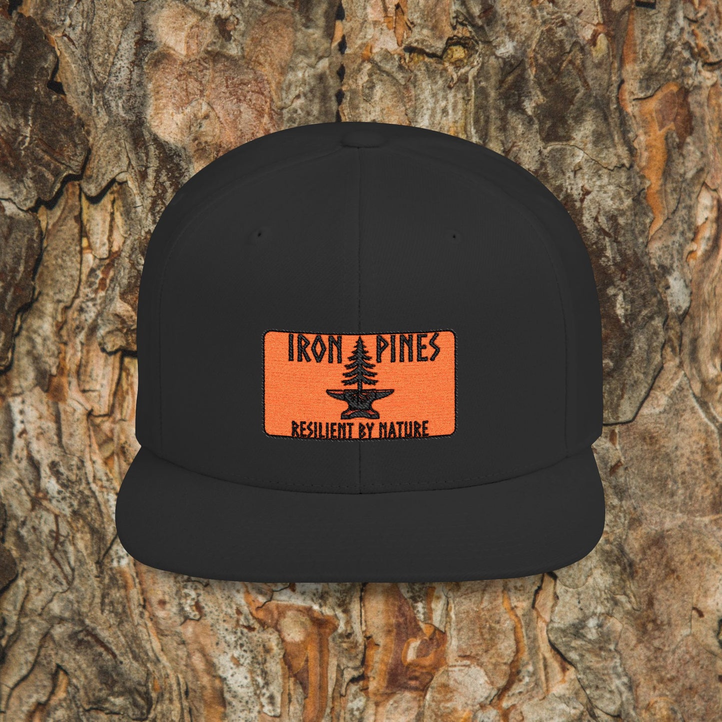 The Iron Pines Logo Hat by Printify is a black structured snapback with an orange patch featuring a stylized pine tree and logo, shown against textured tree bark.