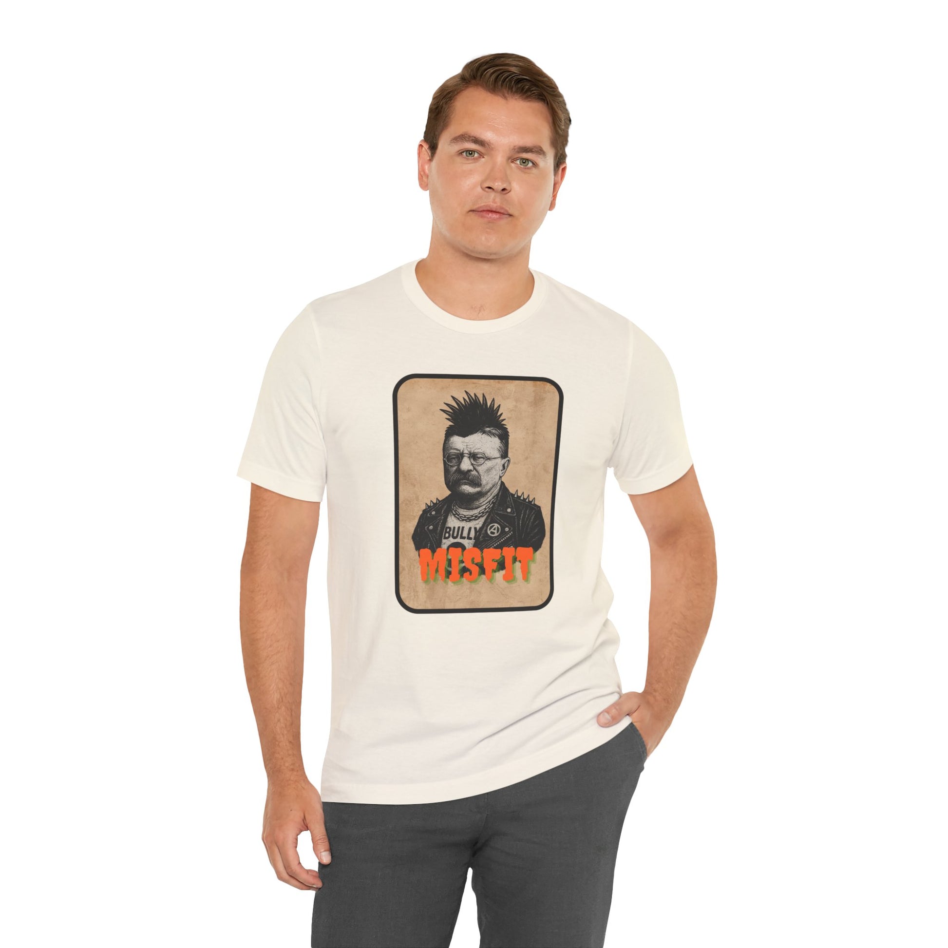 A man wears the Iron Pines Teddy Roosevelt Punk T-Shirt, featuring bold orange “MISFIT” text and a graphic labeled “BULLY,” standing with one hand in his pocket against a plain background.