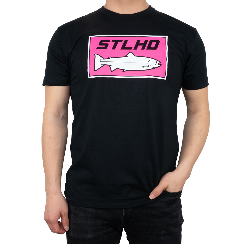 A man wears the STLHD Mens Neon Pink Black T-Shirt by STLHD GEAR, featuring a pink rectangle logo with STLHD above a white fish graphic. He stands against a white background with one hand in his pocket.