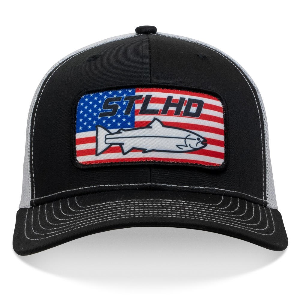 The STLHD GEAR Nation Black/White Trucker Snapback Hat features a patch with an American flag, blue STLHD text, and a wild steelhead silhouette—perfect for dedicated STLHD Nation fans.