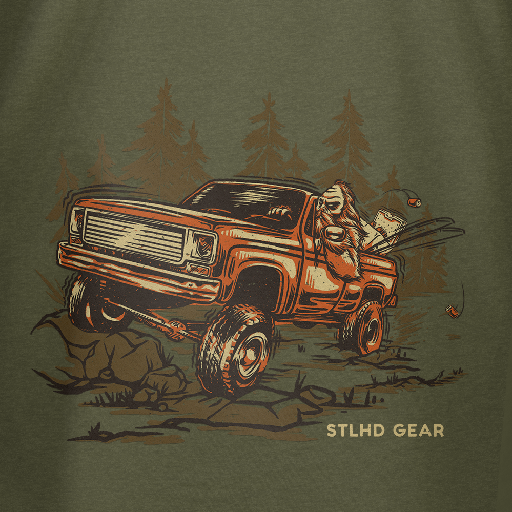 An illustrated bear drives a lifted pickup through a forest, holding a fish. Great for outdoor lovers, the STLHD Men’s 4x4 T-Shirt by STLHD GEAR features “STLHD GEAR” on the bottom right of the image.