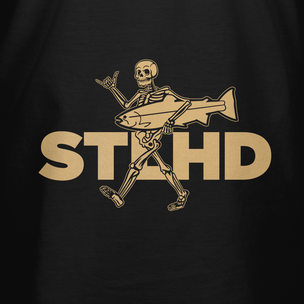 A cartoon skeleton walks with a big fish, flashing a shaka sign, with bold tan STIHD letters on black. The STLHD Loosey Goosey T-Shirt by STLHD GEAR is perfect for fans of chill style and fun fishing-themed graphics.