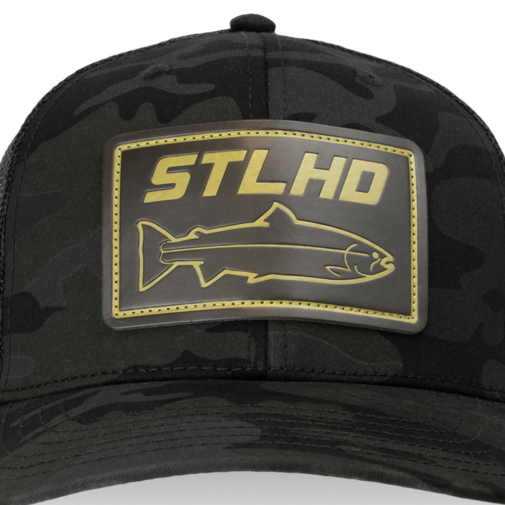 The STLHD GEAR Black Ops Multicam Snapback Trucker Hat features camo fabric, a gold STLHD patch with a fish outline, and an adjustable snapback for style and comfort.