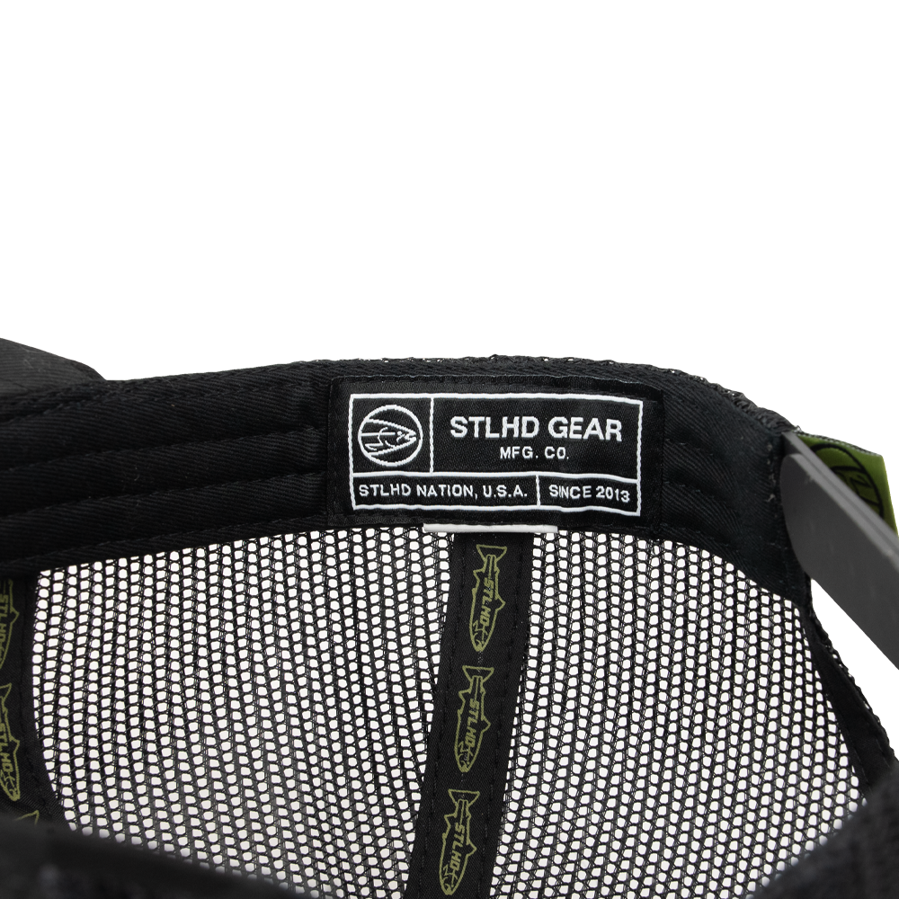 Close-up of the STLHD Black Ops Multicam Snapback Trucker Hat’s interior reveals a label with the STLHD GEAR logo, “STLHD NATION, U.S.A. SINCE 2013,” and a fish emblem. The adjustable snapback features green fish graphics on its inner lining.
