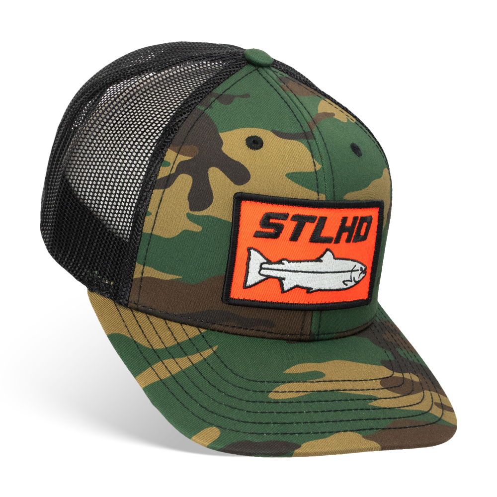 The STLHD GEAR Camo Snapback Trucker Hat features a black mesh back, adjustable snap closure, and a front patch with an orange border, STLHD lettering, and a white fish—ideal for your next fishing trip.