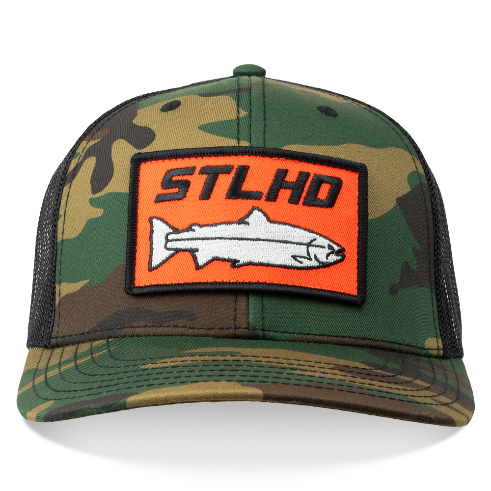 The STLHD Camo Snapback Trucker Hat by STLHD GEAR features a mesh back, adjustable snapback, and a rectangular orange patch with STLHD text and a white fish—ideal for fishing and outdoor enthusiasts.
