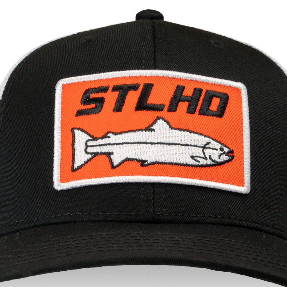 The STLHD GEAR Standard White & Black Trucker Hat features a rectangular orange and white patch with a fish and bold black STLHD text, plus an adjustable snapback for comfort.