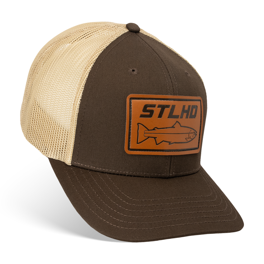 The STLHD GEAR Steelhide Brown/Khaki Hat is a mesh trucker hat with a brown and beige design, a rectangular leather patch displaying STLHD and a fish outline on the front, plus an adjustable snapback for a custom fit.