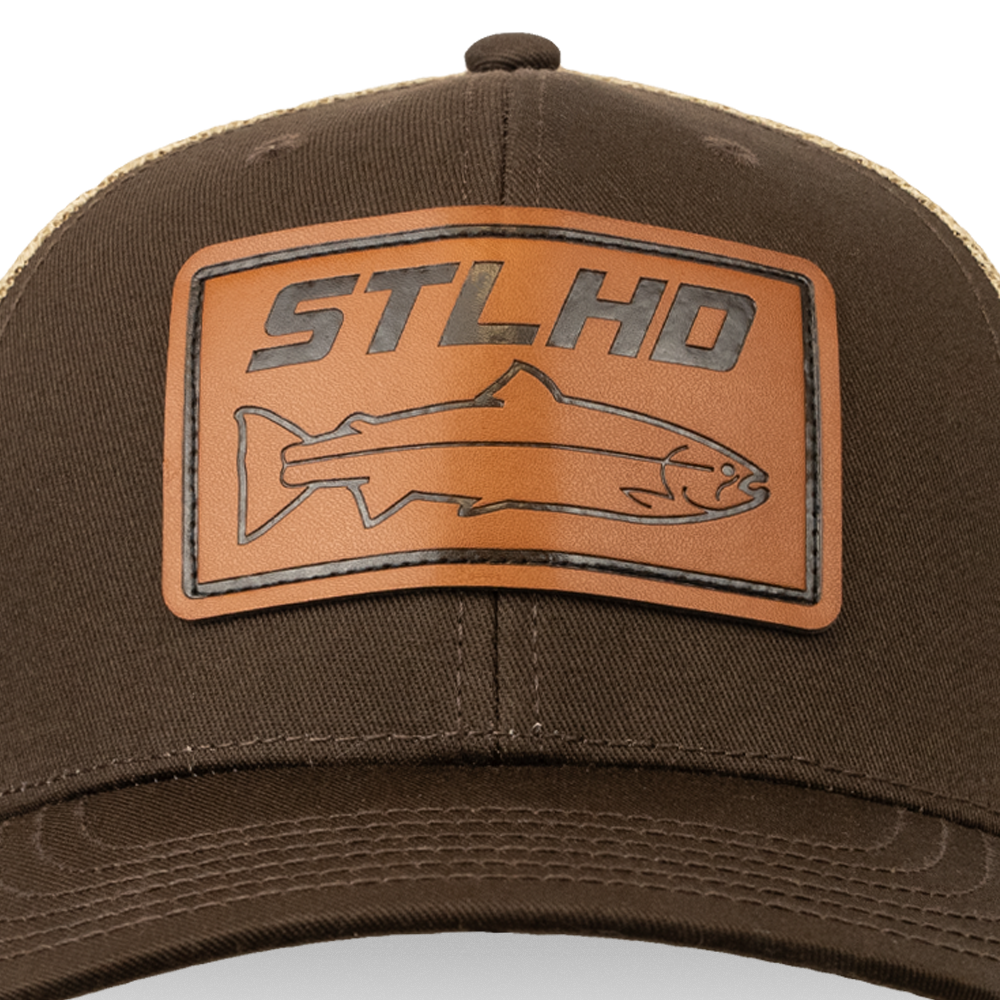 The STLHD GEAR Steelhide Brown/Khaki Hat features a brown leather patch with “STLHD” and a fish outline, an adjustable snapback, and stitched front detailing.