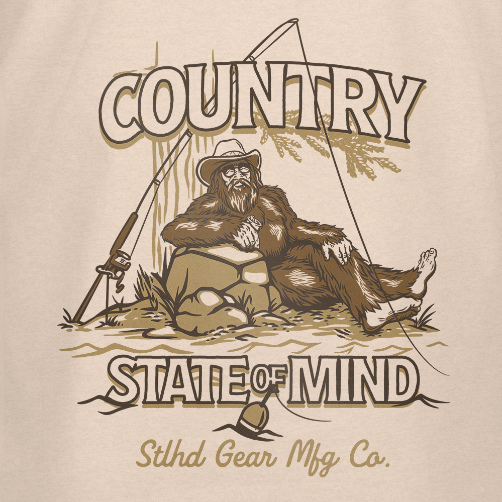Featuring a relaxed Bigfoot lounging by a rock with his fishing rod amid trees and grass, the STLHD GEAR Country State of Mind T-Shirt is perfect for outdoor lovers seeking laid-back adventure vibes.