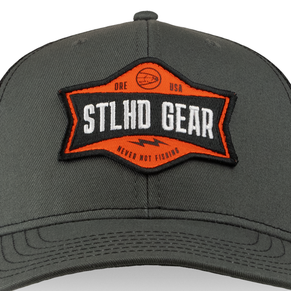 A close-up of the STLHD Never Not Fishing Trucker Hat by STLHD GEAR, a gray fishing trucker hat with an orange and black patch displaying STLHD GEAR, USA, and NEVER NOT FISHING.