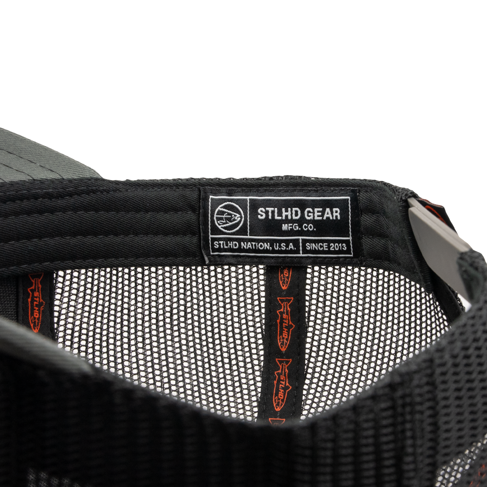 Close-up of the inside of the STLHD Never Not Fishing Trucker Hat by STLHD GEAR, featuring a label with STLHD GEAR MFG. CO. STLHD NATION, U.S.A. SINCE 2013 and branded tape along the seams of this adjustable snapback.