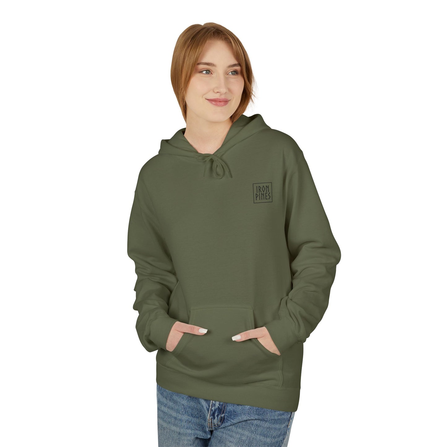 A young woman with light brown hair smiles and looks to the side, wearing The Iron Pines Hoodie by Printify in olive green, made from midweight fleece with a small chest logo. Her hands rest in the pocket.