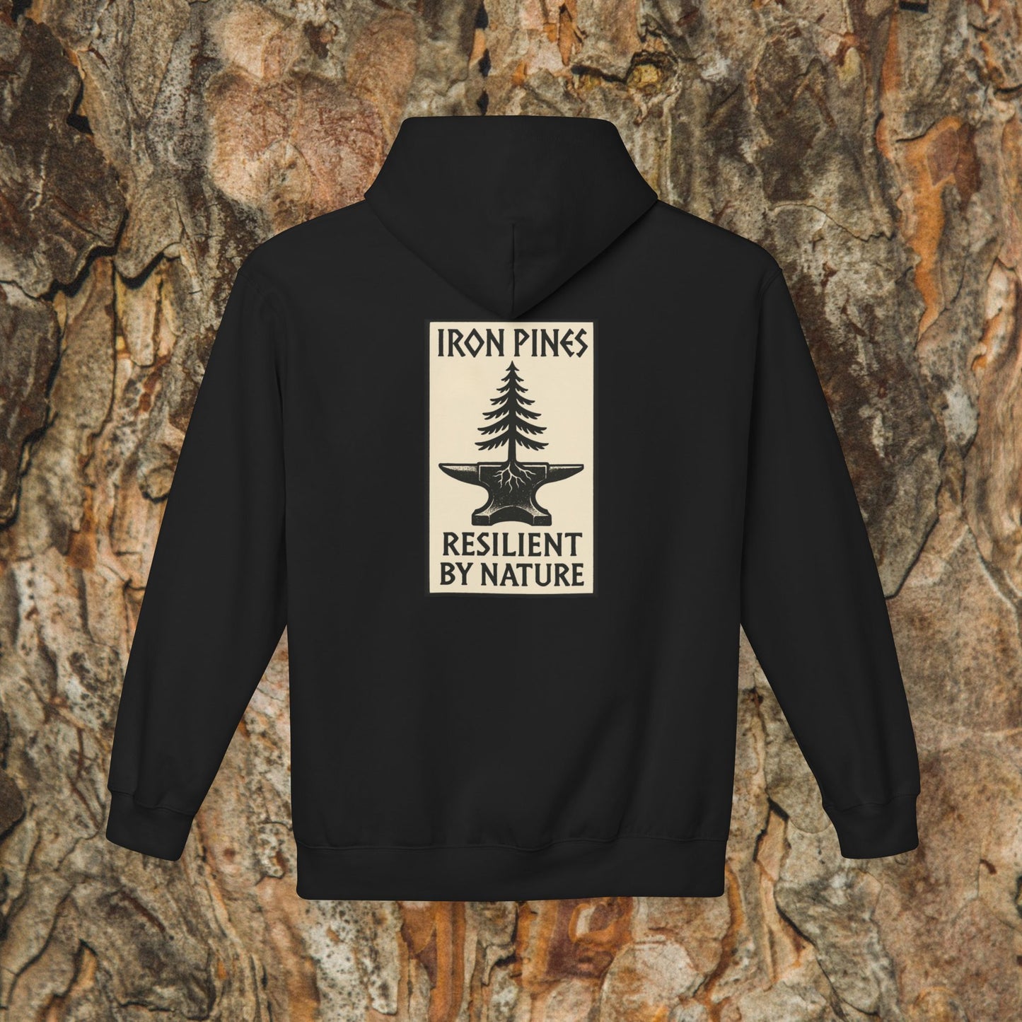 The Iron Pines Hoodie by Printify is a black midweight fleece with a beige back patch featuring a pine tree over an anvil and IRON PINES RESILIENT BY NATURE text. Shown on textured bark, its ideal sustainable outdoor apparel.