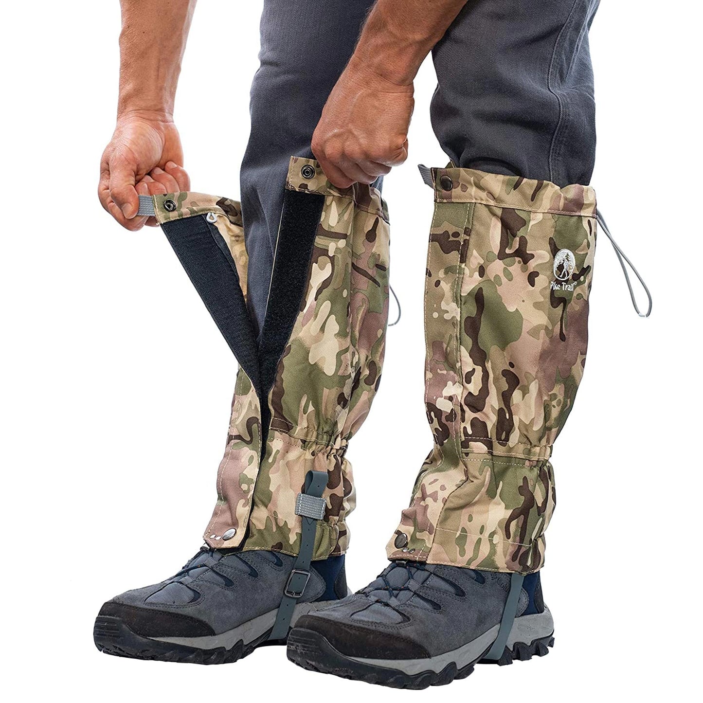 Someone secures Pike Trail All-Season Waterproof Leg Gaiters—abrasion-resistant with Velcro closures, adjustable top cords, and under-boot straps—over gray pants and hiking boots for protection on the trail or during the hunt.
