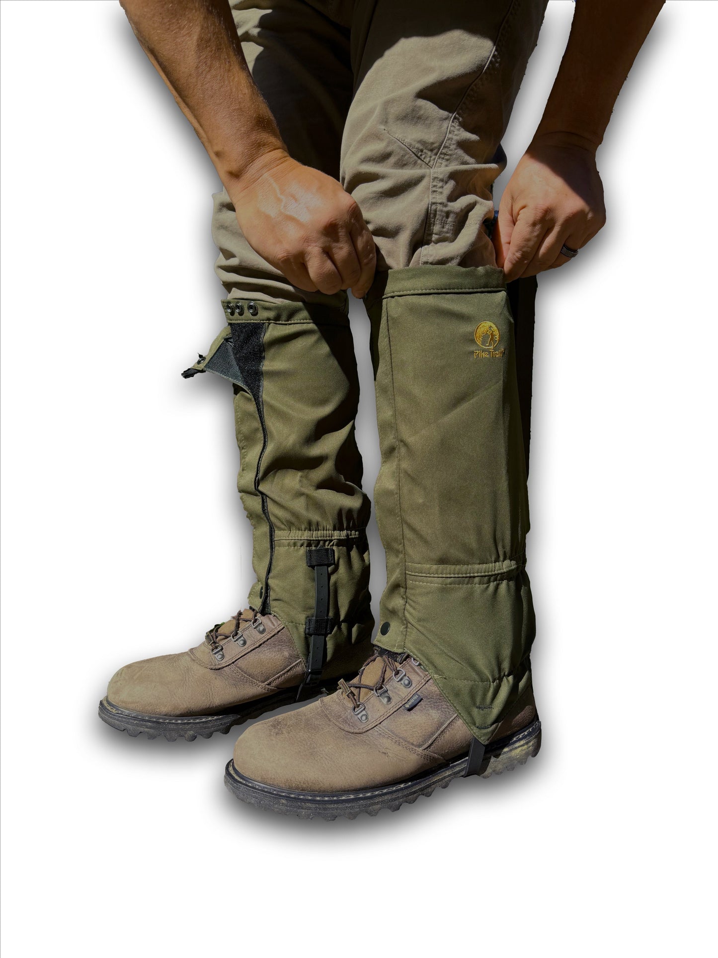A person wearing brown hiking boots and olive green pants is fastening Pike Trail All-Season Waterproof Leg Gaiters—built for the trail, the hunt, and everything in between—over their lower legs for outdoor adventures.