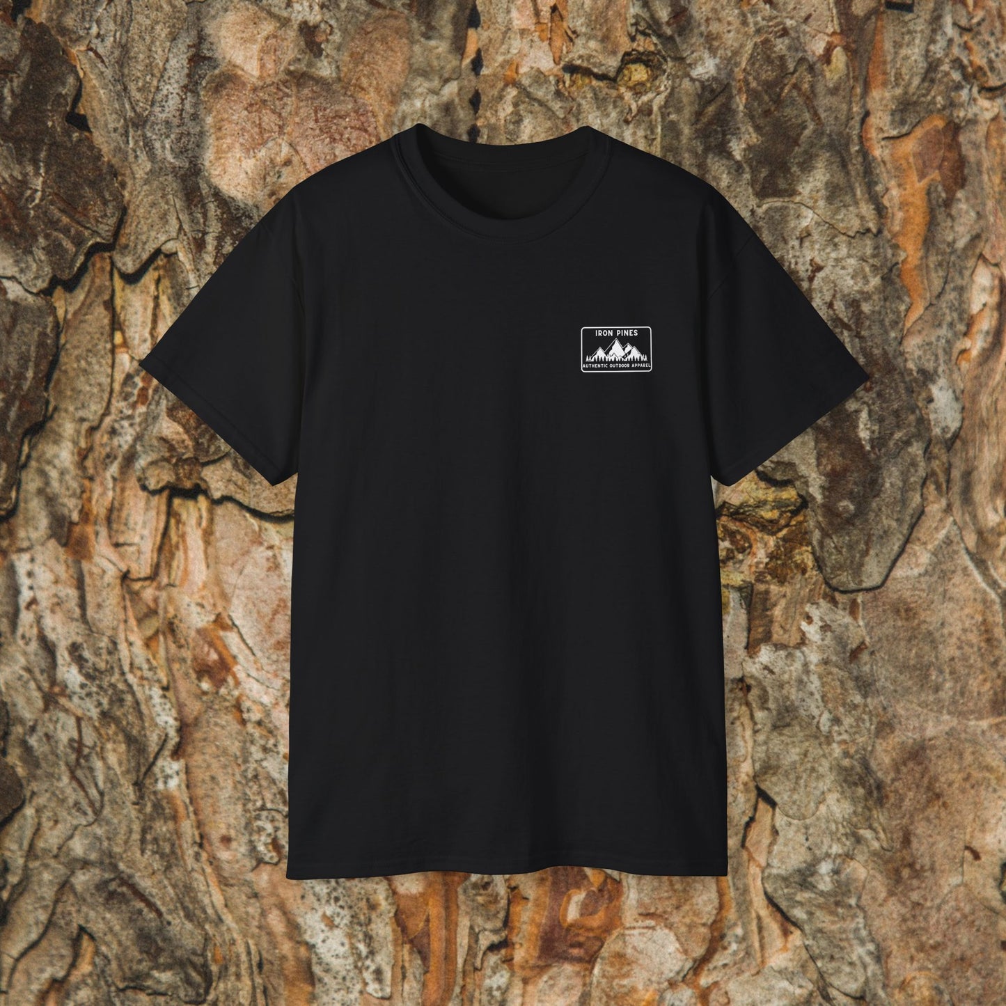 The Iron Pines Public Lands in Public Hands Tee is a black hiking t-shirt with a small white mountain graphic and 180 PINE on the left chest, made from ethically sourced cotton, shown against a textured tree bark background.