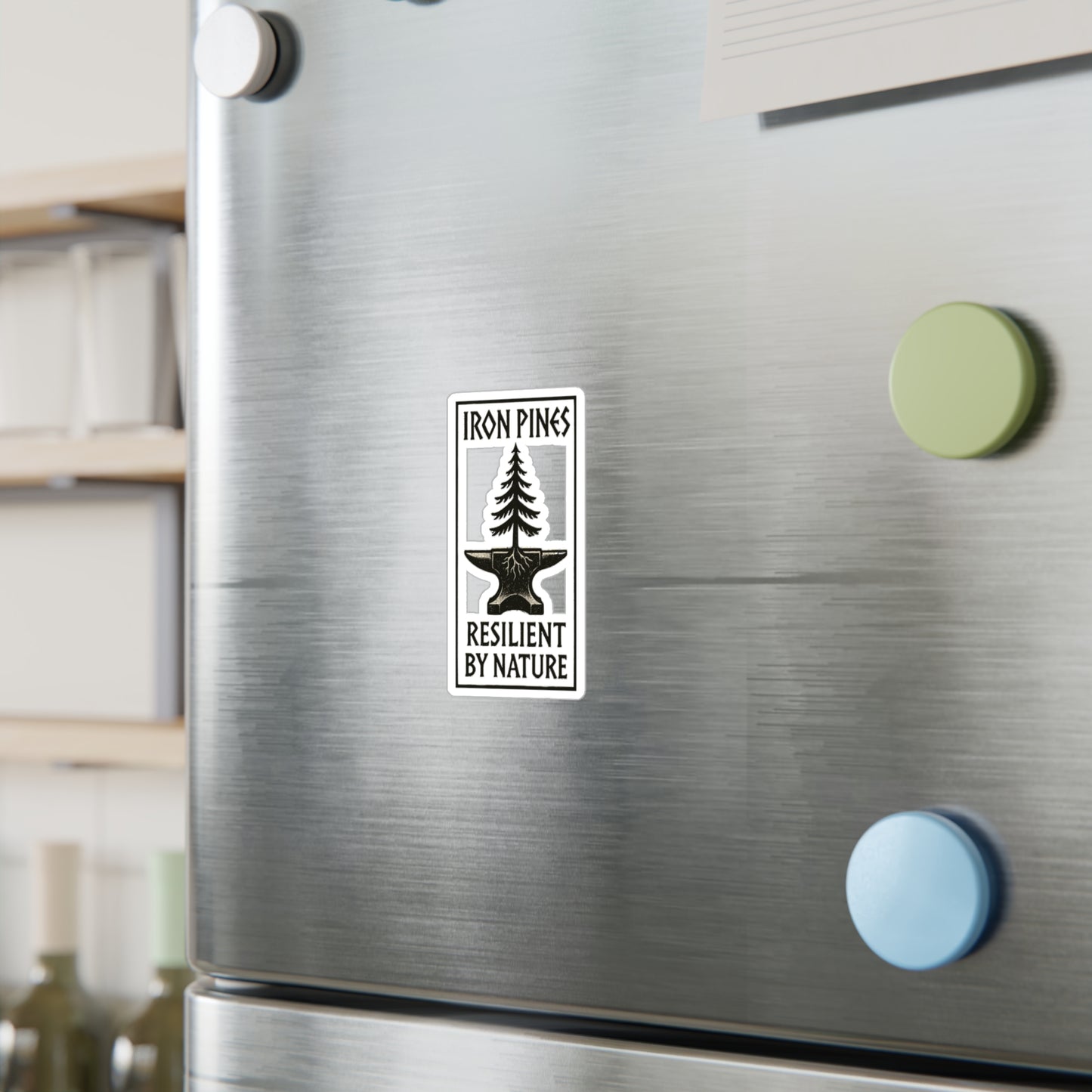 A metallic refrigerator with three round magnets—green, blue, and yellow—and a Printify Iron Pines Logo Sticker – Durable Vinyl with Purpose, reading IRON PINES RESILIENT BY NATURE with a tree growing from an anvil.