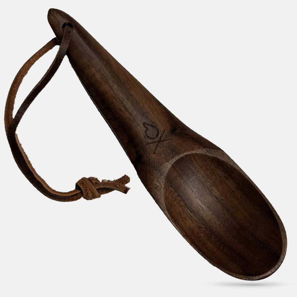 The Überleben Kanu is a handcrafted hardwood camping spoon with a smooth finish, rounded handle, leather loop, and simple engraved design near the scoop—a stylish and eco-friendly utensil by Überleben.