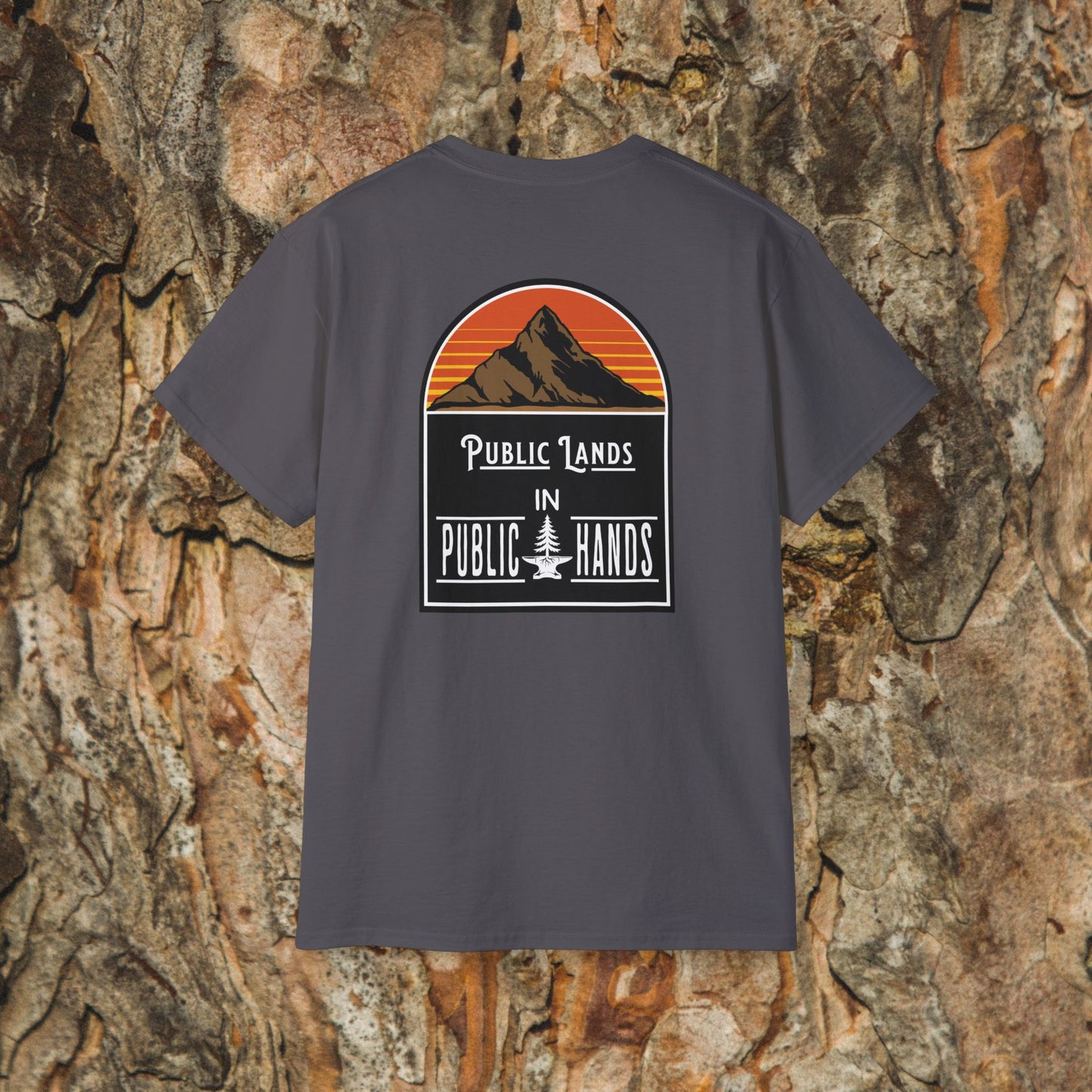 The Iron Pines Public Lands in Public Hands Tee features a sunset mountain and pine graphic with the slogan “Public Lands in Public Hands,” made from ethically sourced cotton, shown against textured tree bark.