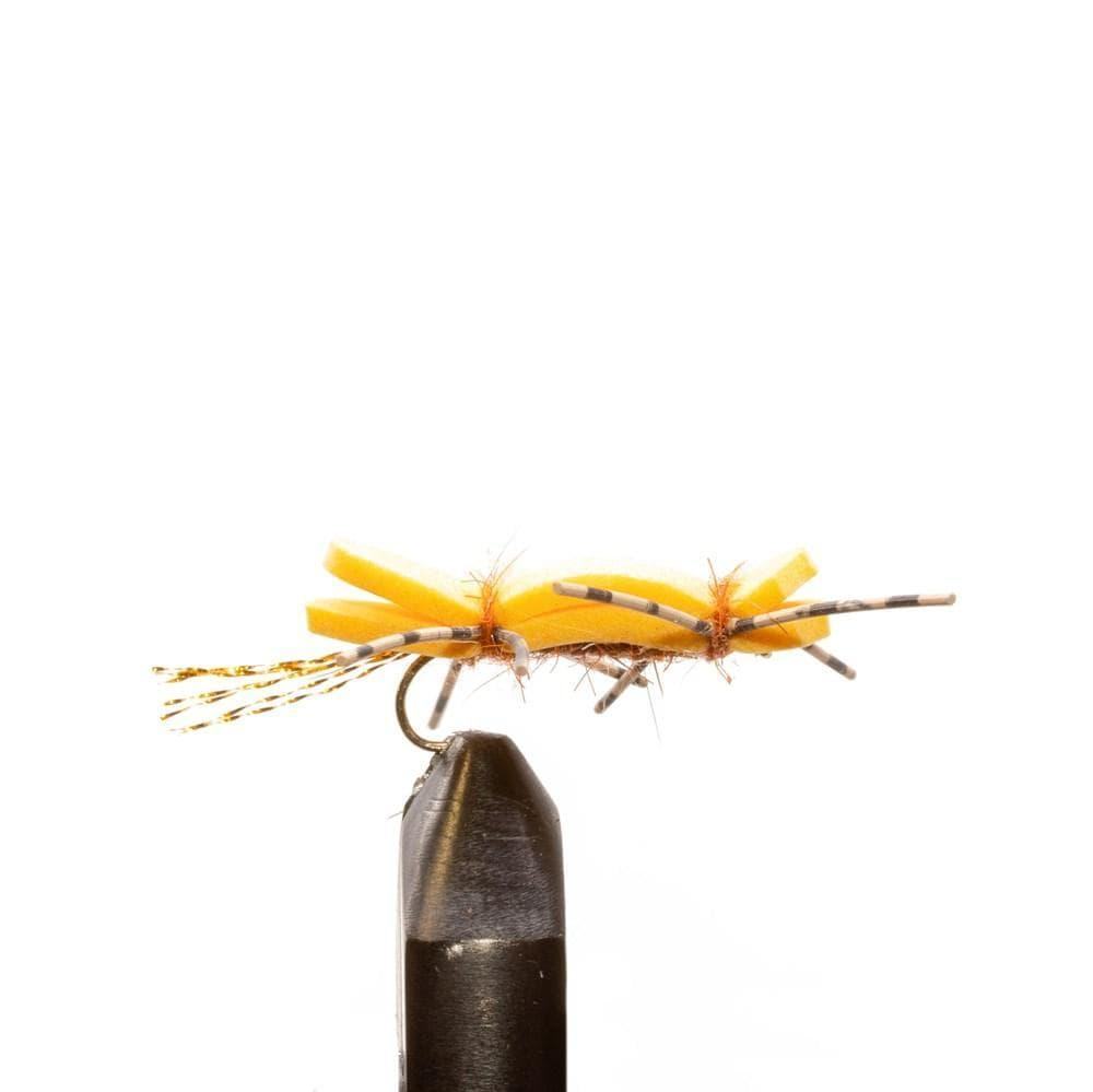 A close-up of a yellow foam fishing fly with speckled rubber legs, mounted on a hook in a vise—ideal for the JHFLYCO Snake River Guides Choice Fly Box by Jackson Hole Fly Company—shown against a white background.