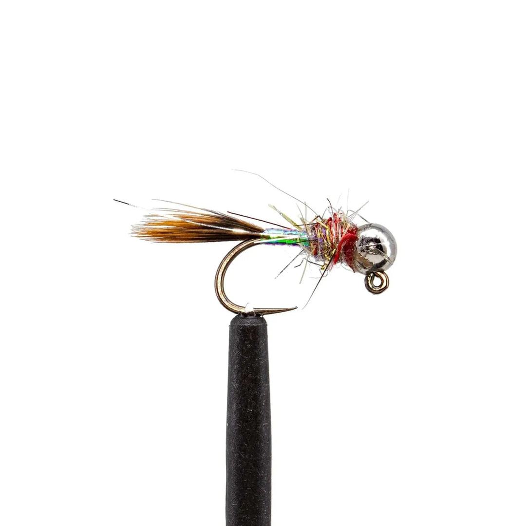 A close-up of the JHFLYCO Loaded Foam Fly Box - Euro Nymph Assortment by Jackson Hole Fly Company shows a tungsten jig pattern fly with a metallic bead head, iridescent body, brown tail fibers, and red thread accents on a black stand.
