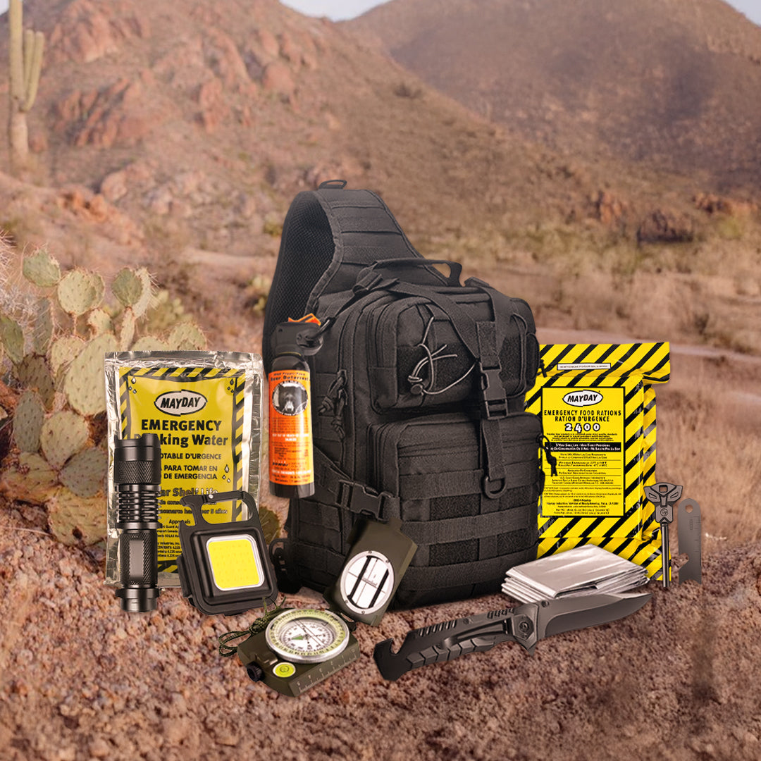 The Entropy Survival Safe Trail “Survive-All” Go Bag, shown in black and surrounded by water pouches, food rations, flashlight, compass, knife, multitool, whistle, and pepper spray, is set against a desert scene with cacti and mountains.
