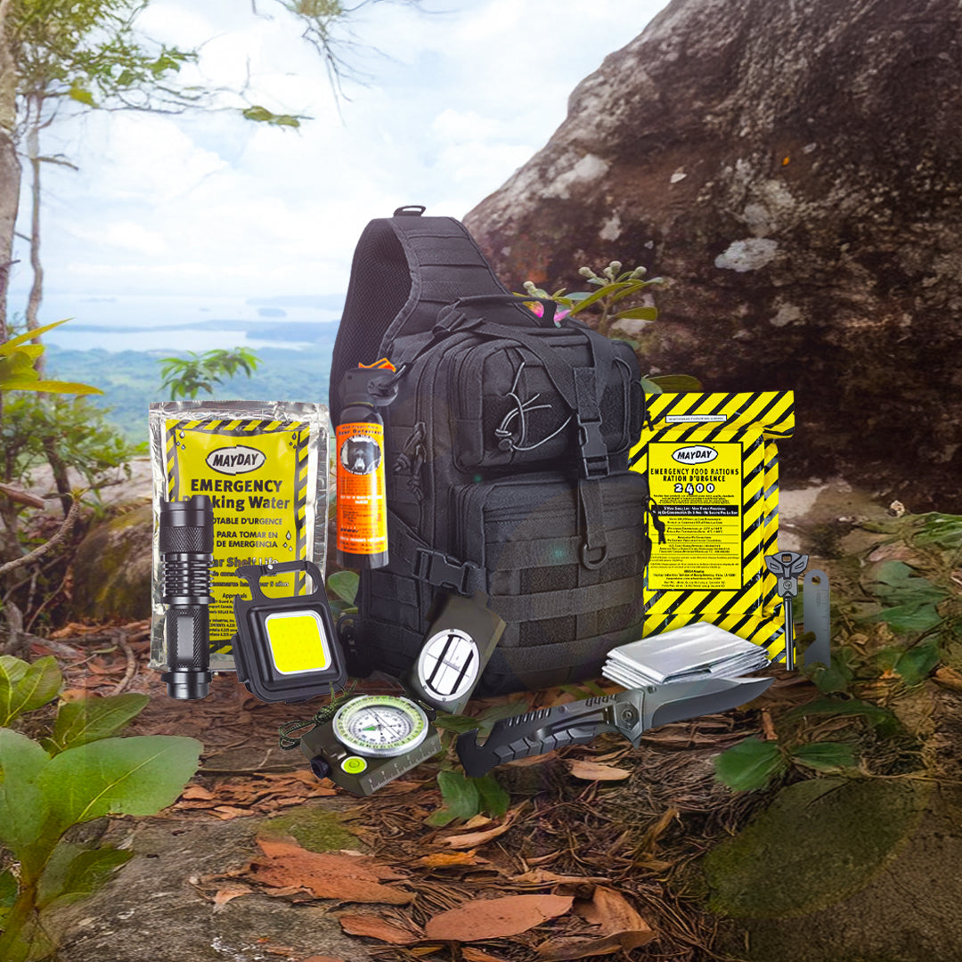 An Entropy Survival Safe Trail “Survive-All” Go Bag in black sits on rugged terrain, surrounded by water pouches, food bars, a flashlight, lantern, compass, multitool, whistle, emergency blanket, and pepper spray.