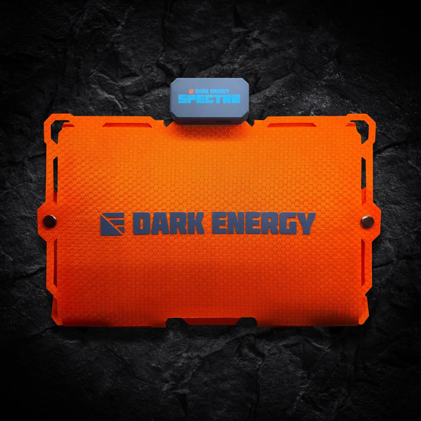 An orange rectangular Entropy Survival Off Grid Survival Power Bundle with a textured finish, plus a small attached blue-gray SPECTRE unit, shown on a dark rocky background.