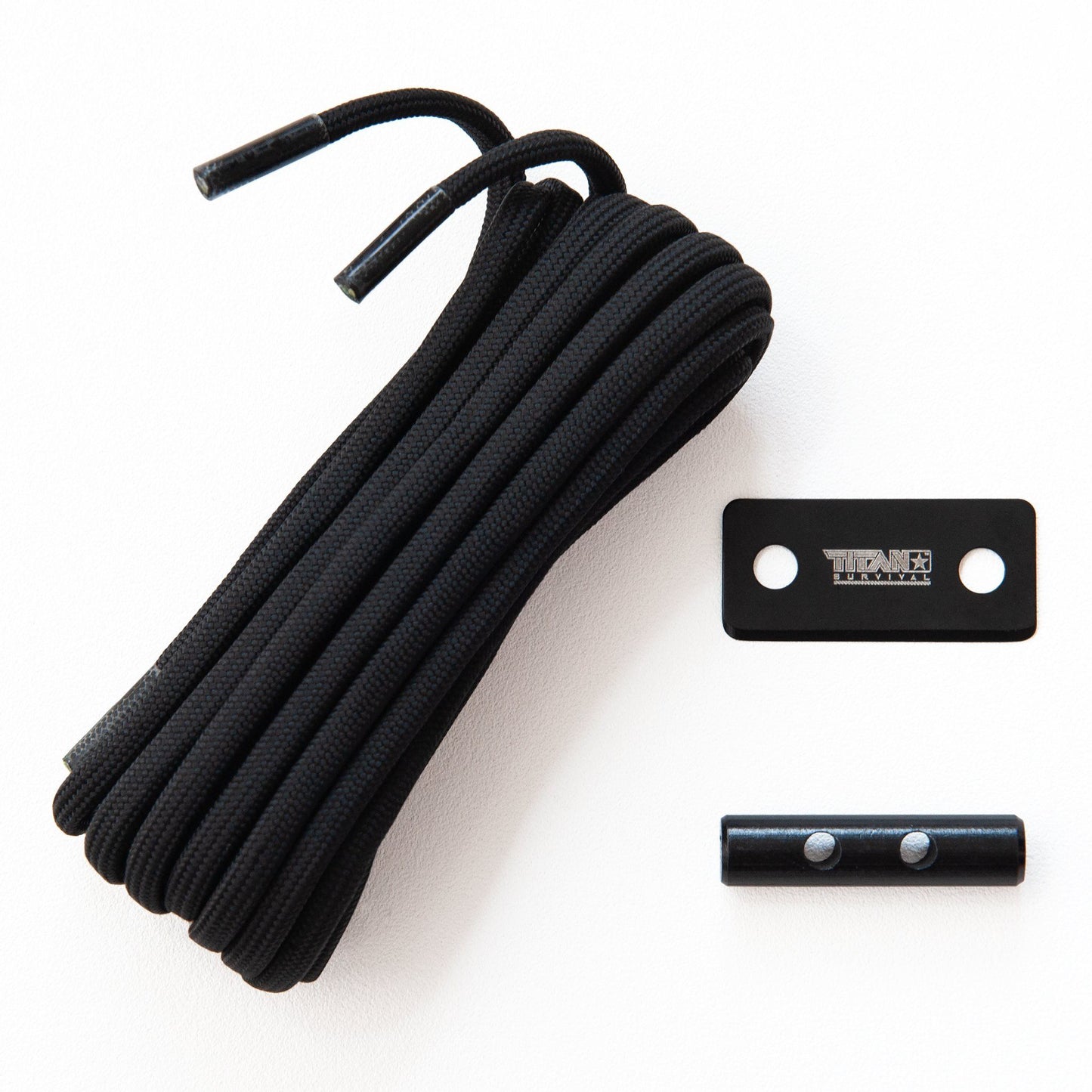A black coiled SurvivorCord® Boot Laces – Firestarter, Kevlar, Fishing Line by TITAN Survival, with a small metal logo plate and a short cylindrical metal tip with screws, are displayed on a white surface.