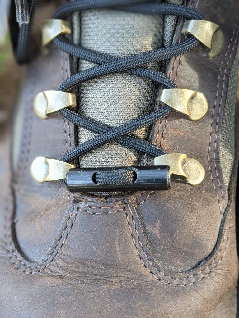 Close-up of TITAN Survival’s SurvivorCord® Boot Laces – Firestarter, Kevlar, Fishing Line, rugged paracord laces in brown leather boots with black laces and plastic lace lock—durable and ready for adventure.