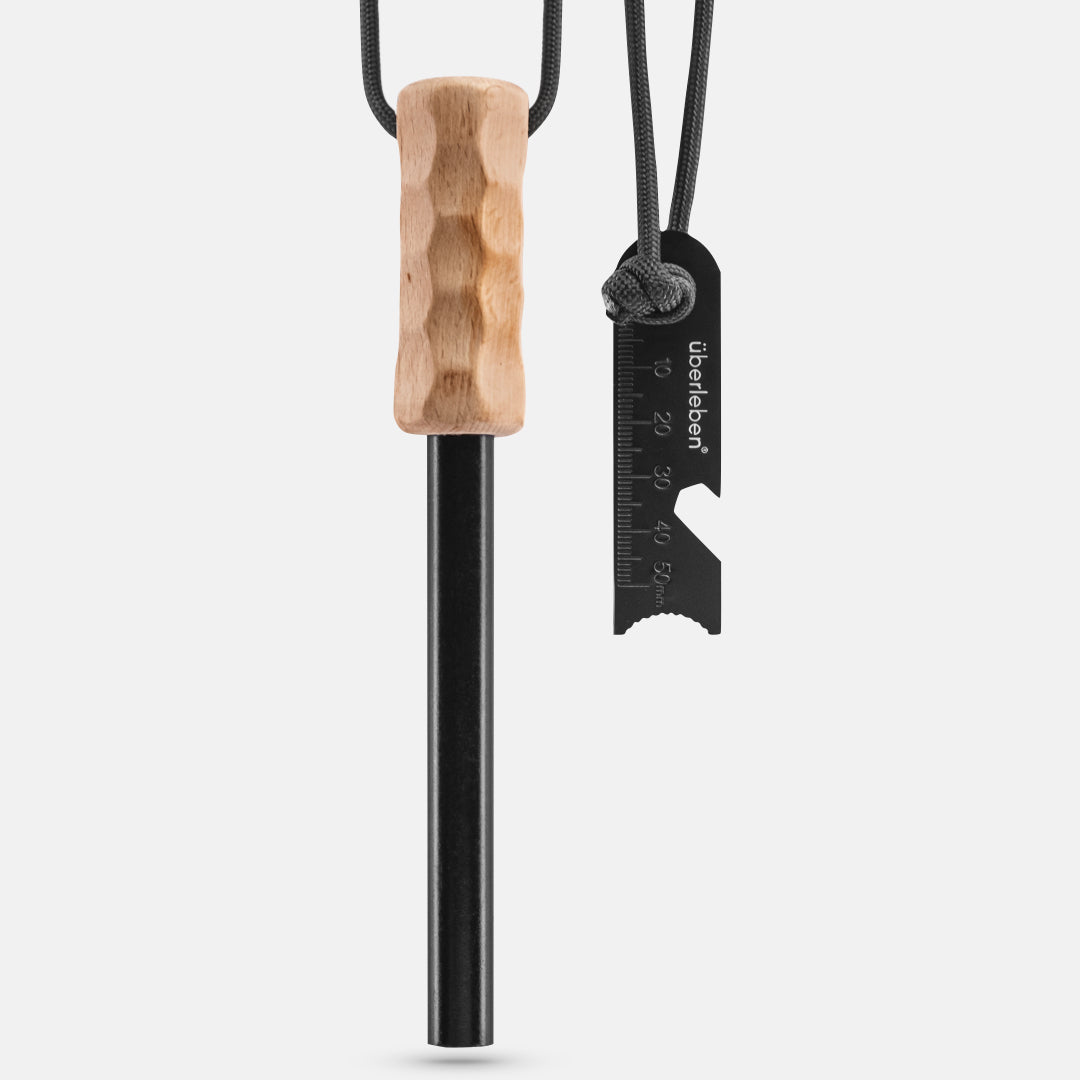 The Überleben Kräftig Grip (PRO) by Überleben is a heavy-duty fire starter with a textured wooden handle, black ferrocerium rod, and multi-tool striker attached by cord, shown on a plain light background.