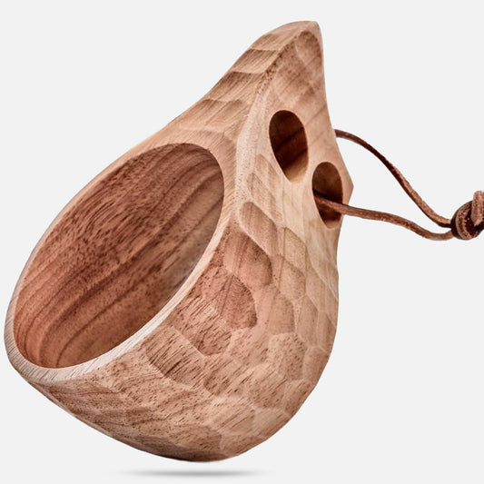 The Überleben Original Kuksa – The Classic Nordic Cup by Überleben is a hand-carved hardwood cup with a faceted surface, two finger holes by the handle, and a leather strap, inspired by Nordic tradition. Shown on a plain white background.