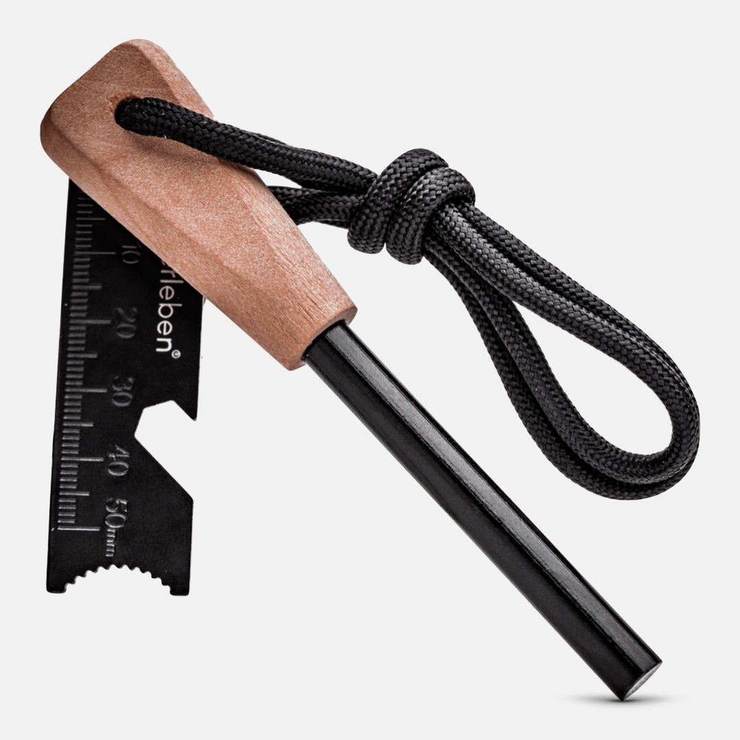 The Überleben Zünden Original – Bushcraft Fire Starter by Überleben features a black ferrocerium rod, wooden handle, metal multi-tool striker with measurement marks, and a black cord—essential survival gear for any adventurer.