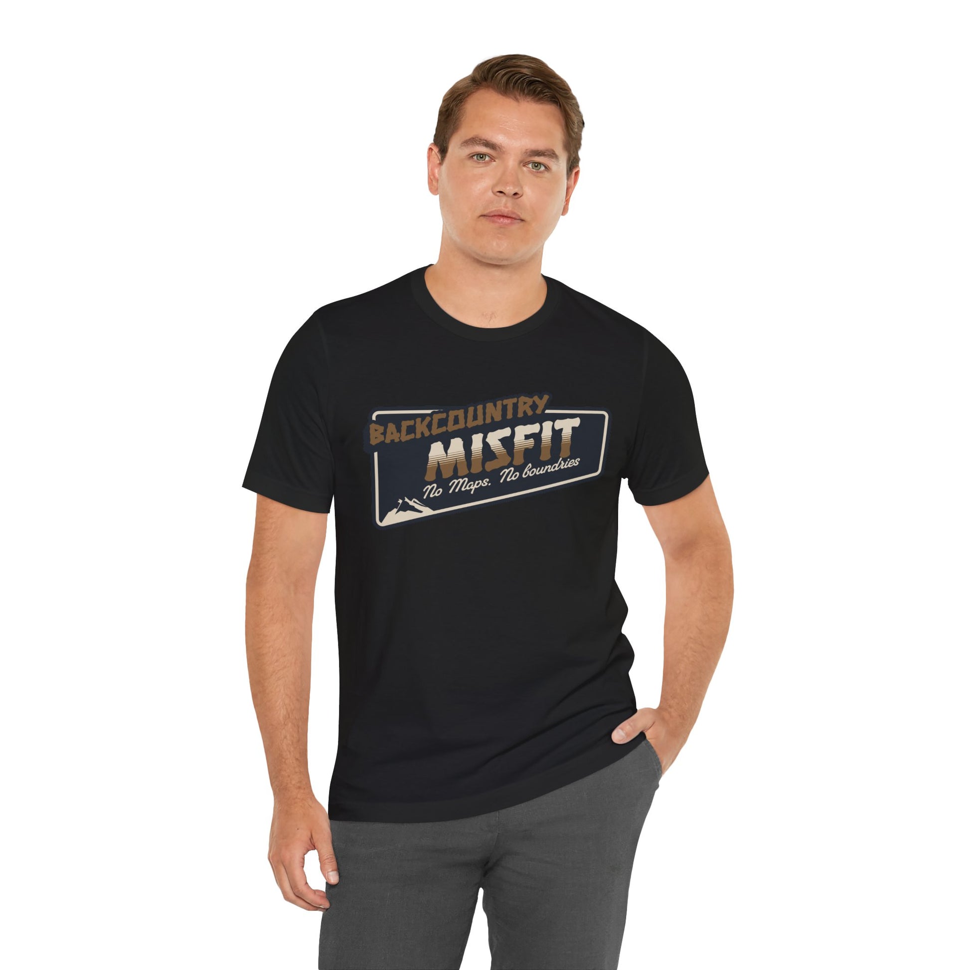 A man with short brown hair wears the Printify Backcountry Misfit T-Shirt, a rugged hiking tee for trail rebels and off-grid wanderers. He stands with one hand in his pocket against a plain white background.