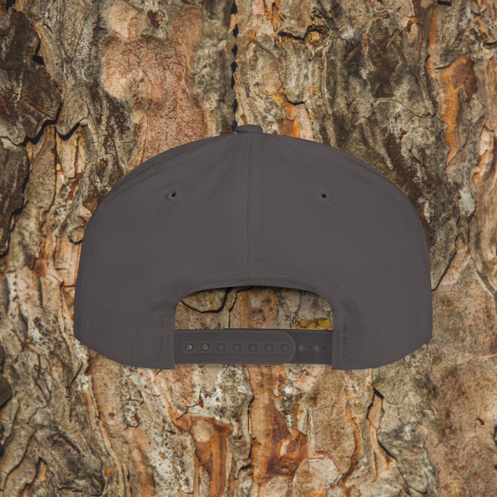 The Iron Pines Logo Hat by Printify is a dark gray structured snapback with an adjustable closure and embroidered logo, shown from the back against textured tree bark.