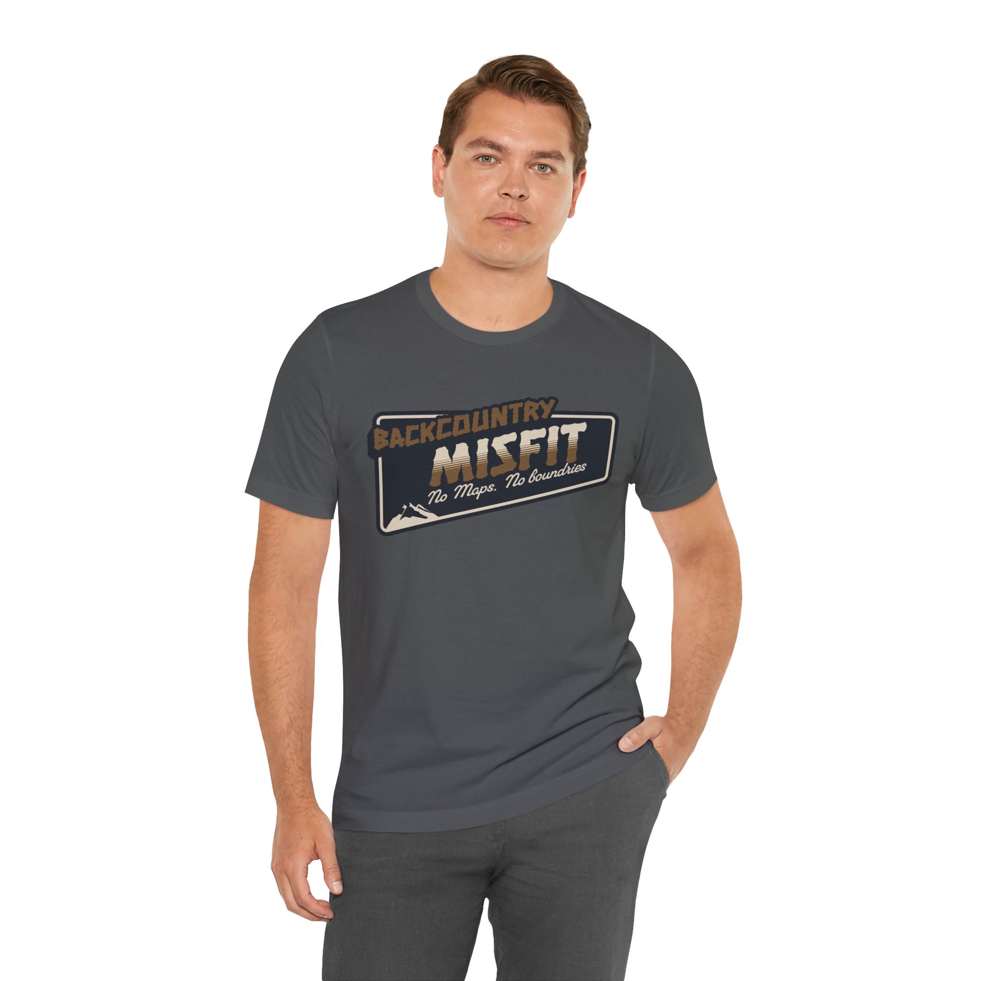 A man stands with one hand in his pocket, wearing the Printify Backcountry Misfit T-Shirt—a rugged hiking tee for trail rebels and off-grid wanderers that declares “Backcountry Misfit – No Maps, No Boundaries” in bold text.