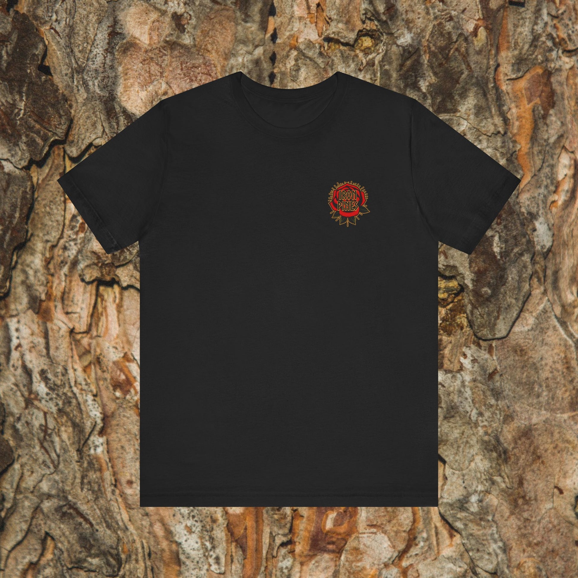 The Never Mistake My Kindness For Weakness Tee by Printify is a black unisex graphic t-shirt with a small circular red and yellow design on the left chest, shown against a textured bark background.